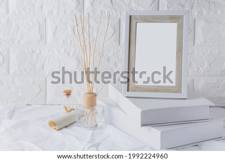 white wood frame Placed on two white books with a white cloth as the background. and has a white wall in the background with branches and paper lying next to
