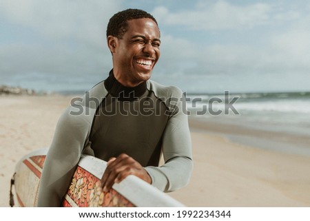 Cheerful man with a surfboard at the beach Royalty-Free Stock Photo #1992234344