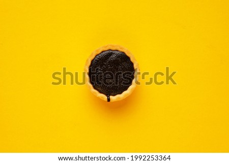 A picture of single homemade chocolate tart on yellow background. Same colour subject and background concept