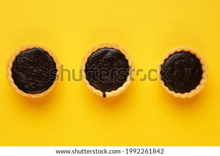 A picture of three homemade chocolate tart on yellow background. Same colour subject and background concept