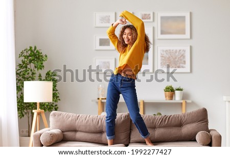 Enjoying freedom. Full length of overjoyed young afro american woman in casual wear jumping and dancing in living room, happy mixed race female teenager spending carefree time having fun alone at home
