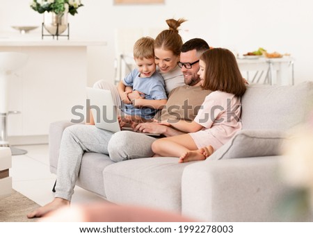 Young happy beautiful family relaxing at home. Father, mother and two children using laptop while sitting on sofa, parents with kids son and daughter watching video or browsing internet together