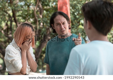 A man, possibly the father or uncle, scolds a younger male, for making his daughter cry. Boyfriend possibly caught cheating. A confrontation outdoors. Royalty-Free Stock Photo #1992290543