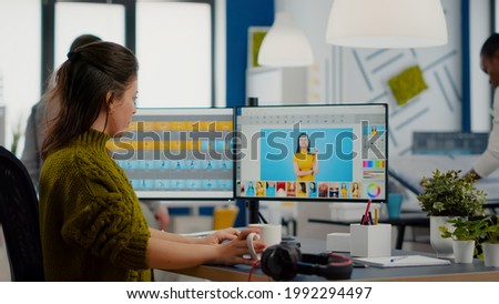 Woman retoucher looking at camera smiling sitting in creative media agency retouching client photos on PC with two displays. Photographer graphic editor working in start up office with digital assets