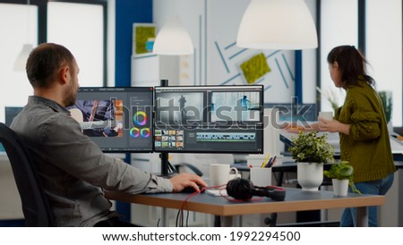 Videographer edits video project and cuts footage and sound using post production software and two monitors taking notes. Man processing film montage in digital multimedia star up company