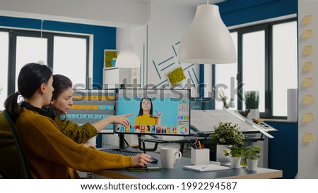 Confident women photo editors sitting in creative workplace retouching photos, art director checking color greding technic talking with worker. Retouchers editing with graphic tablet and stylus pencil