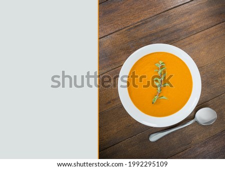 Composition of plate of carrot or pumpkin soup on wooden surface with copy space on grey background. writing background, food and colour concept digitally generated image.