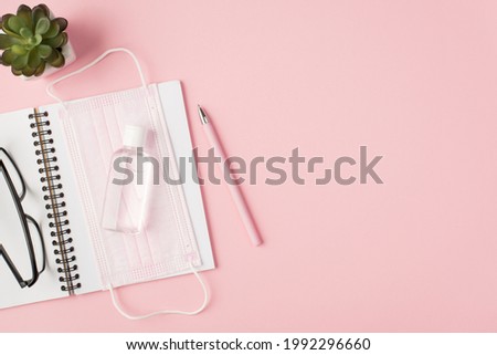 Top view photo of pink medical facemask sanitizer spectacles on open notebook pen and plant on isolated pastel pink background with copyspace
