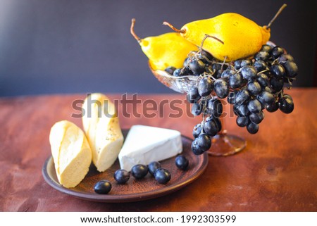 Wonderful food: dark grape brushes, a piece of brie cheese, two pieces of baguette and a few ripe yellow pears