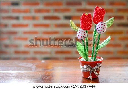 picture of a handmade tulip flower decoration on a teak wood table, with brick wall background.