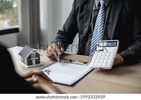 Employees use the calculator to calculate monthly rent for tenants and explain renting details and calculate monthly rent payments to tenants before signing the contract. Renting a house concept. Royalty-Free Stock Photo #1992332939