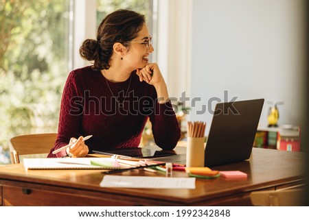 Female artist working from home. Illustrator sitting at home looking away and smiling.