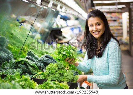 Closeup portrait, beautiful, pretty young woman in sweater picking up, choosing green leafy vegetables in grocery store Royalty-Free Stock Photo #199235948