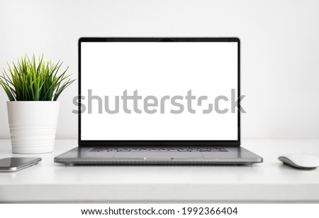 Laptop with a blank screen on white wooden table with mouse, smartphone and grass flower