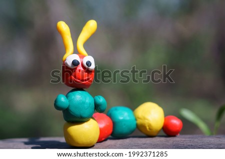 A caterpillar figurine made of plasticine on a background of wildflowers. A symbol of spring.