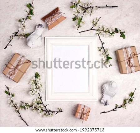 Empty white frame with apple blossom branches, gifts and birds on light marble background. Top view with copy space for text or image.