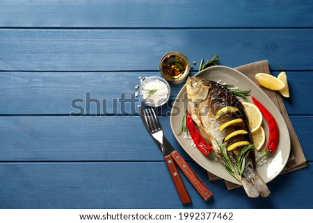 Tasty homemade roasted crucian carp served on blue wooden table, flat lay with space for text. River fish Royalty-Free Stock Photo #1992377462