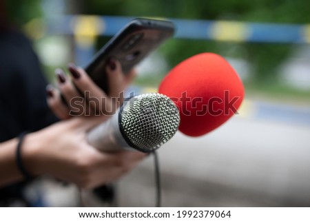 Female journalist at news conference, recording notes, holding microphone and smarthopne lice dictaphone