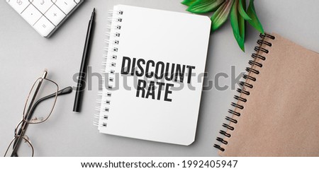 discount rate is written in a white notebook with calculator, craft colored notepad, plant, black marker and glasses.