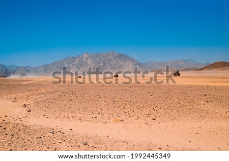 Travelling by quad over desert sand. Safari riding four wheel ATV bike driving to adventure. 
Off road Driving through rocky dry desert