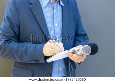 Journalist at news conference or media event, holding microphone, writing notes. Broadcast journalism concept. Royalty-Free Stock Photo #1992480380