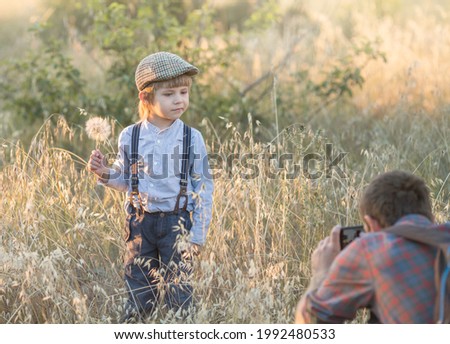 dad takes pictures of his son in nature on his mobile phone. the child is holding a white dandelion