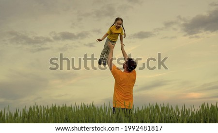 Little happy child flies like an airplane against the background of the sky in green wheat, the concept of a happy family with dad, cheerful children's life, kid laughs in the hands of his father