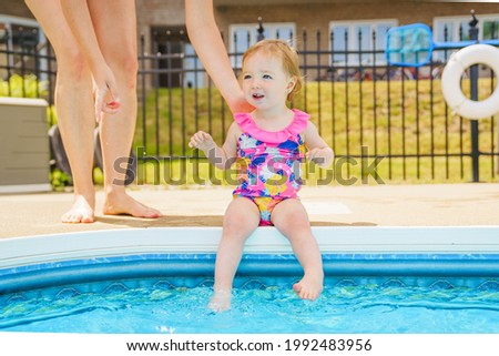 Child girl is sitting in the pool with mother look for the security