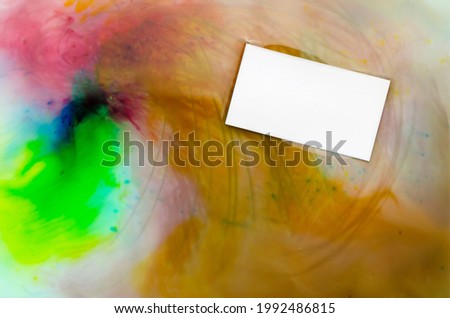 Blank white business card on a multicolored abstract background. Rectangular business card floating in water with mixed watercolors. Business concept. Top view. Selective focus.