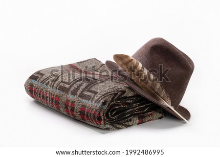 Christmas gift, woolen throw blanket in Pendelton style and hat with feather on white background.