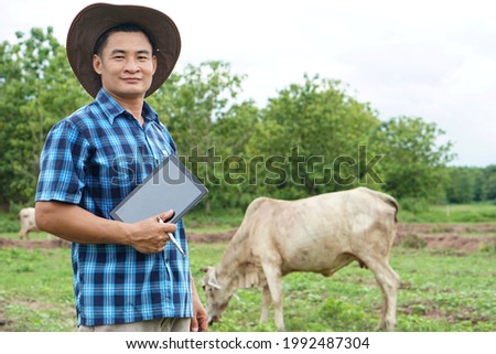 Livestock and technology concept ; Asian male farmer is taking care his cattle and use smart tablet to record information about growth and disease of animal.