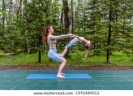 Mother and daughter doing yoga on grass in the park at the daytime. People are having fun outdoors. Concept of candid family and summer vacation.