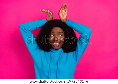 Photo portrait of woman smiling showing bunny ears with hands looking blank space isolated on vibrant pink color background