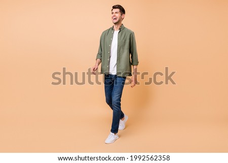 Photo of funny handsome young gentleman wear khaki shirt walking laughing smiling isolated beige color background Royalty-Free Stock Photo #1992562358
