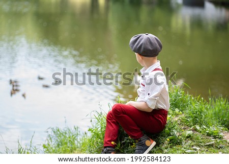 Boy in a cap sits by the pond