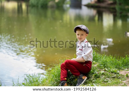 Boy in a cap sits by the pond