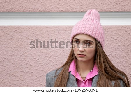 Portrait of a young girl outdoors on a blurred background of a wall painted pink. An attentive mistrustful angry and attentive judgmental look. High quality photo. Copy space.
