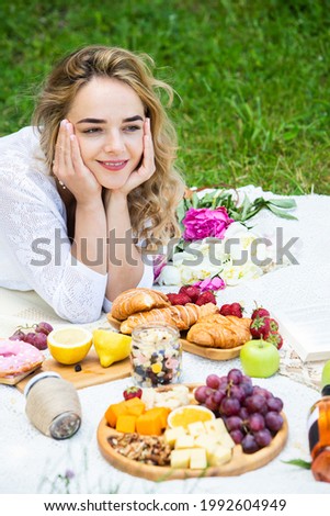 Beautiful woman resting in park sitting on a picnic blanket with fruits and wine. 