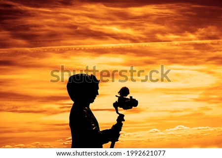 Silhouette of videographer is filming with cinema gimbal video dslr , professional video, videographer in events. Cinema lens on gimbal. side view. Film or cameraman school