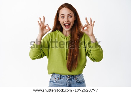 Impressed smiling girl with red hair, shows okay OK sign and look amazed, praise cool promo offer, make compliment, show zero gesture, white background