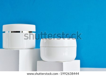 White jars of cosmetics on a white podium on a blue background. Bath accessories. Face and body care concept. Set of professional cosmetics for face and body. Copy space.