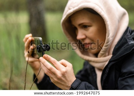 Phone lenses for macro photography. A woman holds a mobile phone with a macro attachment in her hands and takes pictures of plants.
