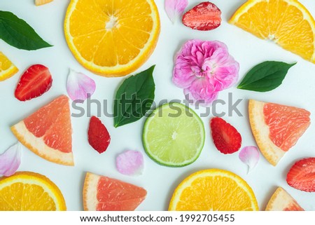 Fruit tropical background. Top view, mockup of tropical fruits on white background: orange, grapefruit, lime, strawberry, tea pink rose and jasmine leaves. Summer bright background. Food concept