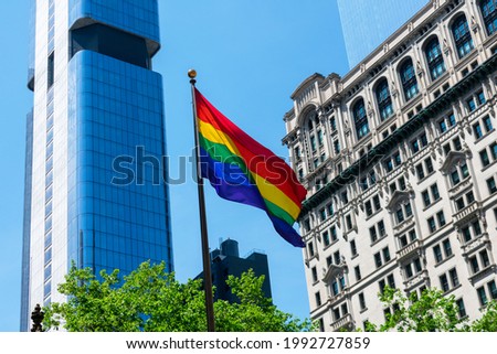 Rainbow Pride Flag proudly flying, waving in the wind. High rise old and modern skyscrapers background in Downtown Manhattan.