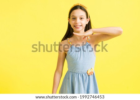 Feeling pretty and beautiful with my looks. Charming little girl posing with a new dress and making a big smile in front of a bright yellow background