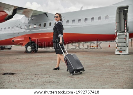 Stewardess walk with baggage on runway near plane