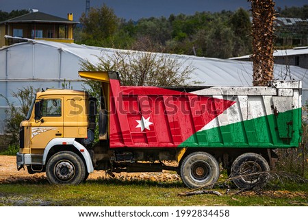 Dump truck with the image of the national flag of Jordan is parked against the background of the countryside. The concept of export-import, transportation, national delivery of goods