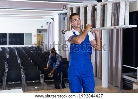 Man and woman in overalls preparing conference hall for event