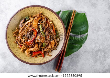 Plate of asian buckwheat soba noodles with vegetables, mushrooms and chicken on light gray background top view
