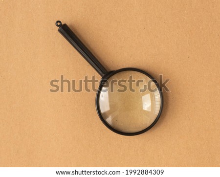 Magnifier or magnifying lens over brown carton background. Search tool.